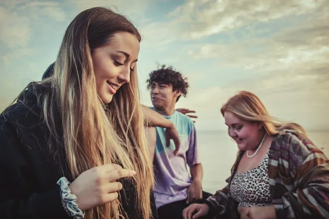 Three young people laughing together on a coast at sunset.